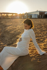 A young pregnant woman is walking on the beach in the evening. The concept of motherhood and childbirth