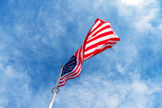 Low-angle view of the national flag of the United States of America waving on a flagpole against blue sky