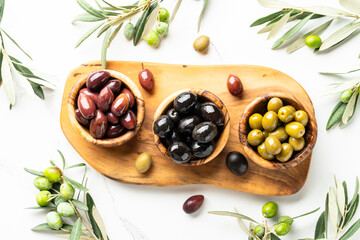 Olives in wooden bowls and Olive oil in the bottle at white table.