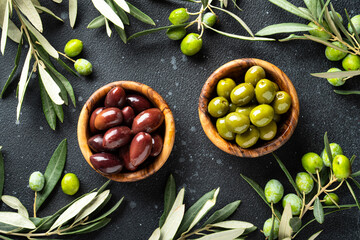 Olives in wooden bowls and Olive oil in the bottle at black table.