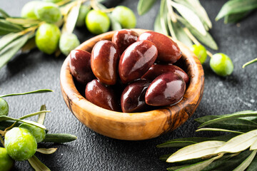 Olives in wooden bowl at black background.