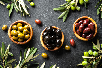 Olives in wooden bowls and Olive oil in the bottle at black table.