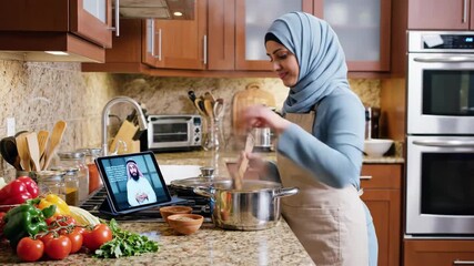 Muslim woman in a hijab cooking in a modern kitchen. Following an online video recipe on a tablet. Preparing a traditional halal meal for Ramadan
