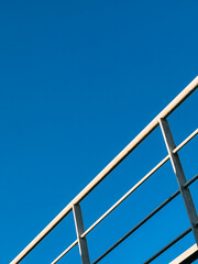 Diagonal white metal railing lines on blue sky background
