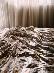 Unmade Bed with Floral Sheets and Sunlight Shadows in Cozy Bedroom
