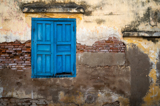 Blue wooden window on an old weathered wall with peeling paint and exposed bricks - Powered by Adobe