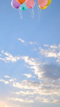 Group of children at sunset release colorful balloons above a green meadow. Balloons float higher into warm clouded sky as camera tilts up, leaving generous copy space.
