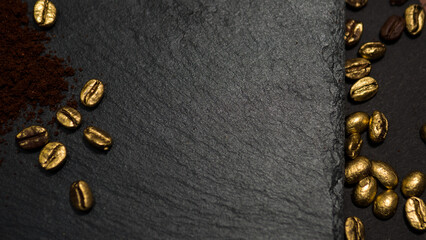 Minimalist flat lay of golden coffee beans scattered on a dark stone surface with ground coffee...