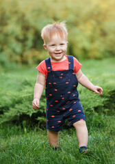 The boy is taking his first steps and laughing. Happy kid boy is standing on the grass in the park in the summer. Protection kids from insects