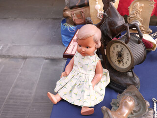 Vintage items and toys at flea market in Europe, Italy. Doll in dress and table clock. Old items and art. 