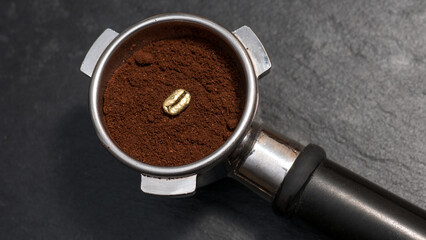 Top view of an espresso portafilter filled with ground coffee featuring a single golden coffee bean...
