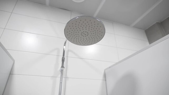 Round overhead shower head shines gently inside clean tiled public booth. Soft diffuse reflections create soothing refreshing atmosphere