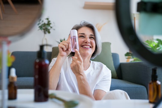 Happy woman presenting toner bottle during beauty tutorial at home