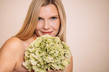 Blonde woman holds a bouquet of green hydrangeas close to her face, showcasing natural beauty and elegance, with a soft neutral background enhancing the serene atmosphere