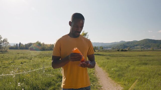 African American man protecting his skin while enjoying a walk in the countryside, applying sunscreen, medium close up shot.