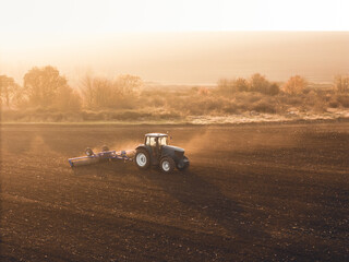 Fototapeta premium Agricultural concept, a tractor plow a field at sunset golden hour. Aerial Top view