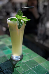 Refreshing beverage in tall glass garnished with fresh mint leaves, placed on a textured green tile surface, showcasing a vibrant drink for summer enjoyment and relaxation