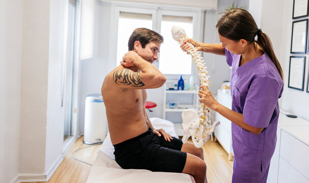Chiropractor showing spine model to patient during consultation in clinic