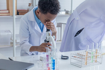 Cute African boy elementary students kids wearing lab coat using microscope attention dropping liquid substance into flask glass in laboratory classroom, lifestyle learning education in science class