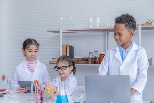 Group of multicultural African boy and elementary students girl kids friend wearing lab coat uniforms using microscope with teacher in laboratory room, lifestyle learning education in science class