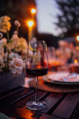 Elegant wine glass filled with red wine, surrounded by soft candlelight and floral arrangements on a rustic wooden table, creating a warm and inviting dining atmosphere