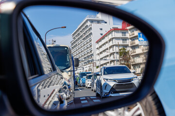 都会の渋滞と街並みを映し出す走行中の車のサイドミラー