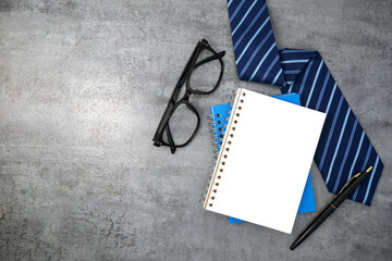 Necktie with notebook and glasses on stone texture background. Business desk office. Top view