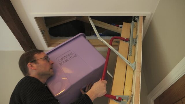 4K: A Man putting away the Christmas Decorations in a box into the Loft or Attic. Stock Video Clip Footage.