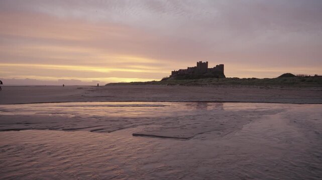A low-angle static wide shot of the majestic Bamburgh Castle silhouetted against a golden sunrise sky
