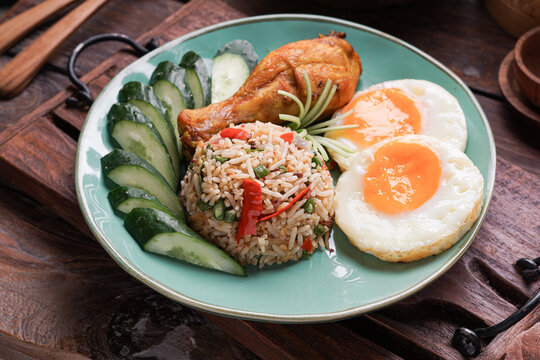 Nasi Goreng served with fried egg fried chicken and fresh cucumber ulam is a classic Southeast Asian meal combining savory flavors, crispy textures, and traditional home cooked comfort food.