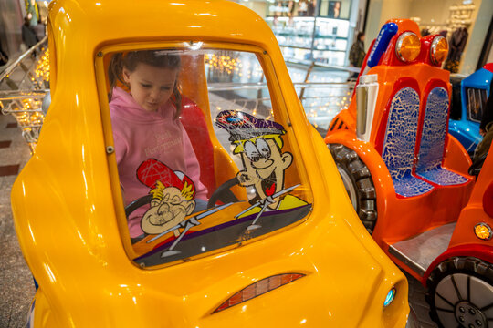 Little girl riding coin operated toy car attraction in shopping mall kids area. Childhood entertainment moment, family leisure activity and everyday fun experience in real life commercial environment