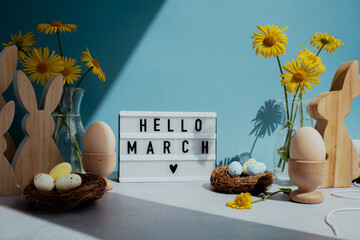 Phrase HELLO MARCH traditional greeting to christian holiday. Festive mood composition with bunnies and yellow flowers on pastel blue background. Sustainable natural materials decorations