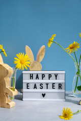 Happy Easter text on Lightbox with bunny wooden figures and fresh flowers. Easter composition content still life. Christian symbols of spring holiday 