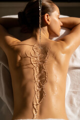 Woman lying on spa table with water flowing over back and towel draped on surface