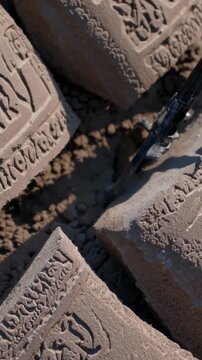 Multiple clay bricks with inscriptions lie scattered on a construction site, creating a repetitive pattern, suggesting ongoing building activity