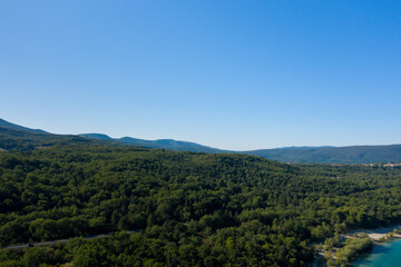 Fototapeta premium Expansive view of densely forested hills near Lac de Sainte-Croix, with vibrant greenery stretching toward distant mountain ridges beneath a cloudless sky.