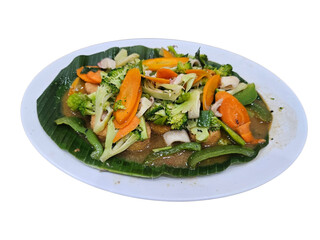 A vibrant stir-fried vegetable dish with broccoli, carrots, and green beans, served on a banana leaf on a white plate, showcasing healthy Asian cuisine.