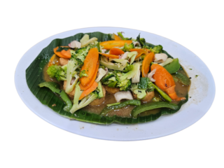 A vibrant stir-fried vegetable dish with broccoli, carrots, and green beans, served on a banana leaf on a white plate, showcasing healthy Asian cuisine.