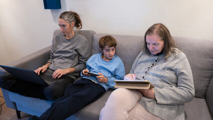 Family members using digital devices on sofa at home