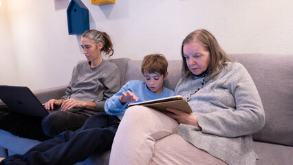 Multi-generational family members using digital devices on sofa