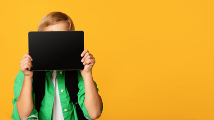 Adolescent blond male pupil show tablet with empty screen, isolated on orange background, panorama....