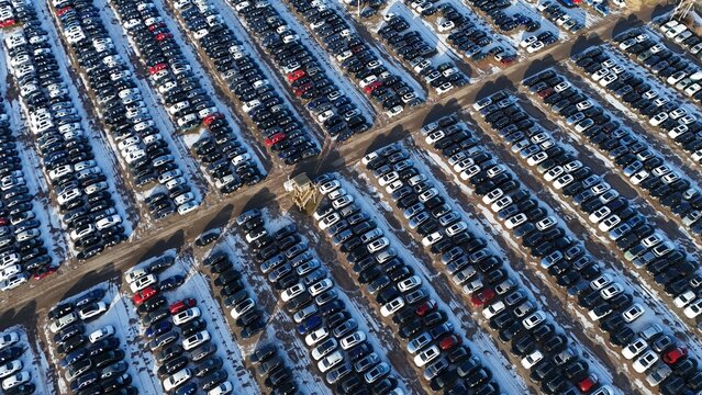 Aerial view of a vast car park, a geometric tapestry of vehicles interspersed with patches of snow, casting long shadows under the winter sun, Corby, England, United Kingdom.