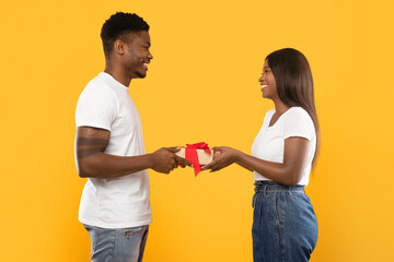 Obraz premium Two individuals are exchanging a gift. The man hands a wrapped present to the woman. They both are smiling and appear happy. The background is bright yellow and simple.