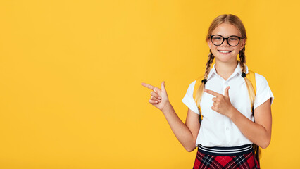 Smiling cute smart adolescent blonde hemale pupil in glasses shows fingers to empty space, isolated...
