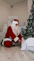 Fototapeta premium Santa Claus carefully places a gift under the Christmas tree surrounded by presents