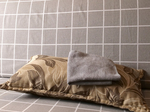 Decorative patterned pillow with folded gray towel on a checkered sofa near a wall, cozy indoor still life.