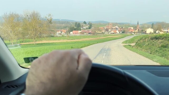 POV view of rural road in Alsace with village houses and church ahead seen from car interior captured as cinematic movie 4k real scene footage during countryside drive