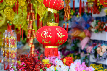 A vibrant red lantern decorated with gold calligraphy and fireworks motifs hangs among festive decorations at a market in Ben Tre, Mekong Delta, southern Vietnam. The scene features rich textures © Florent