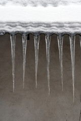 Icicles hang from the edge of a snow-covered roof during winter in a cold climate