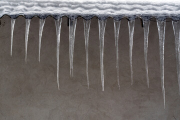 Icicles hang from an eave on a cold winter day near a gray wall